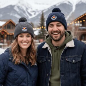 A man and woman wearing Colorado Mountain Brewery pom-pom beanies in a snowy mountain town. in Colorado Springs Colorado