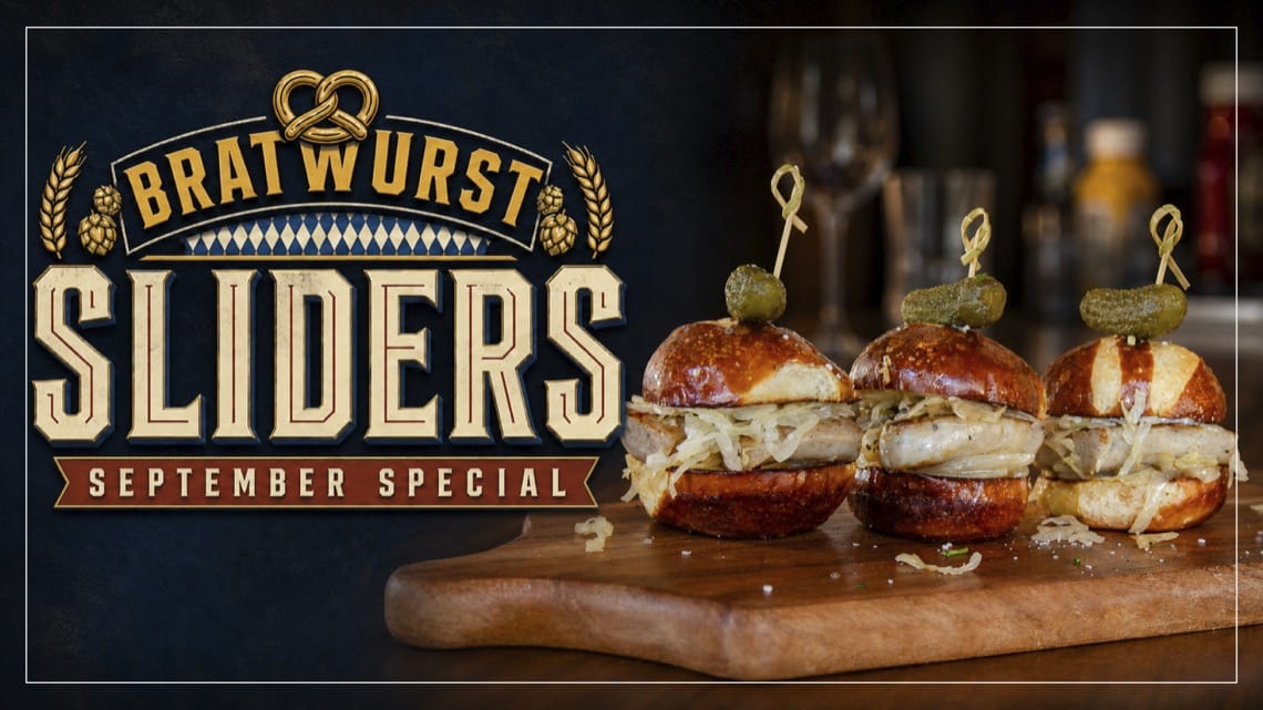 Three bratwurst sliders on pretzel buns with sauerkraut and pickles on a wooden board. Colorado Mountain Brewery September special.